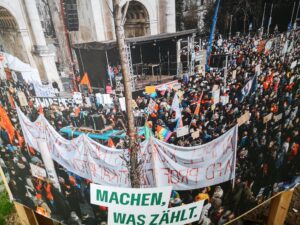 In München plakatiert die Grüne Partei im EU-Wahlkampf ein Foto von den Anti-AfD-Protesten. Im Vordergrund ein Transparent gegen die Ampel-Regierung, deren Teil die Grüne Partei ist.